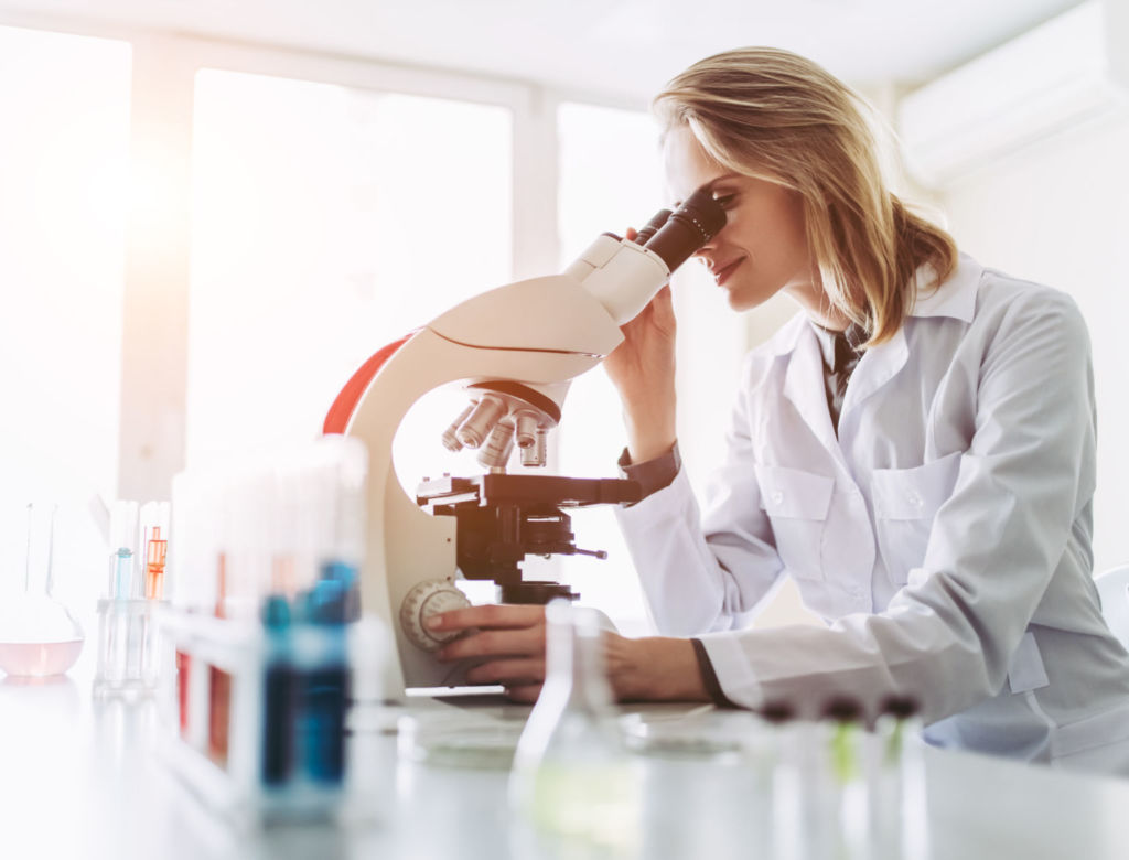 Experienced female scientist is working in laboratory. Doing investigations with microscope.